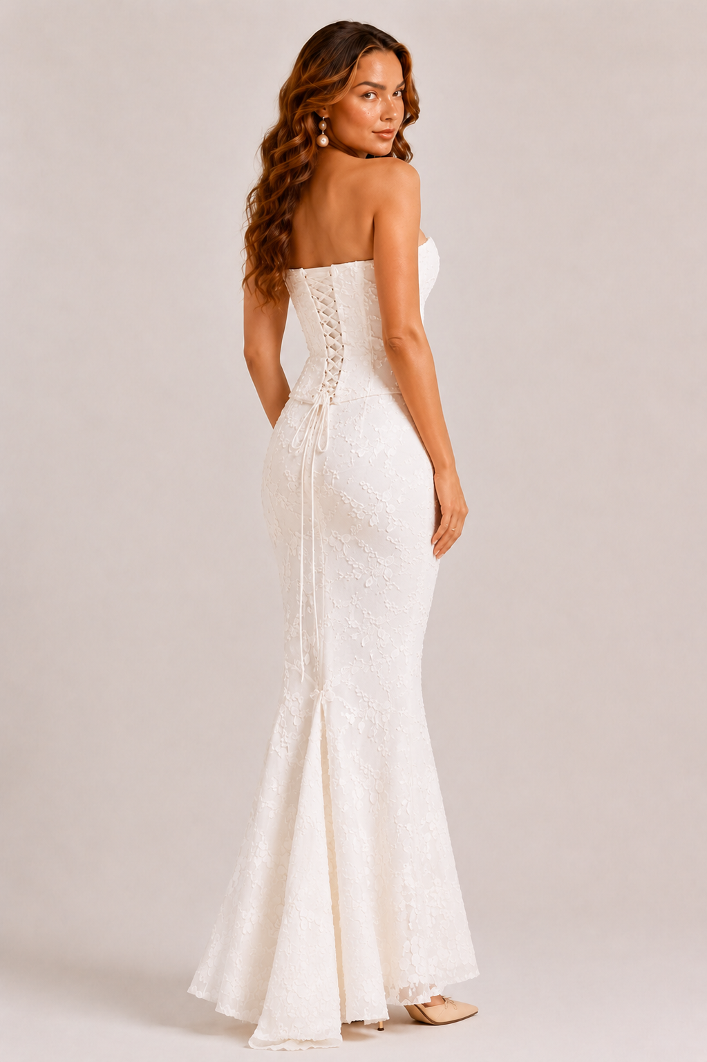Woman wearing a white strapless gown with a fitted design on a plain background