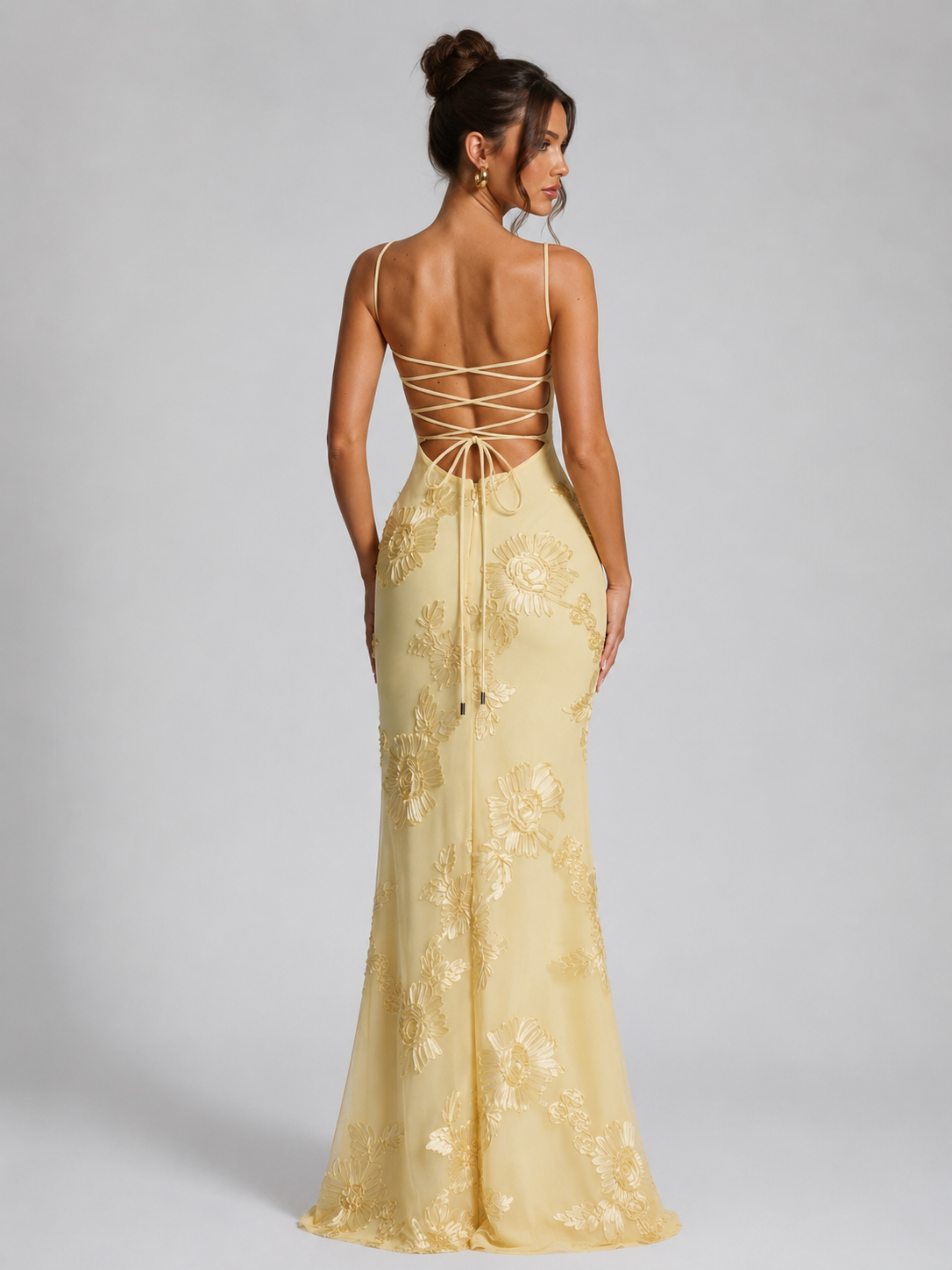 Woman wearing a yellow lace evening gown with a backless design on a gray background