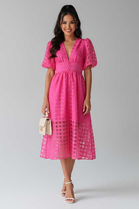 Woman wearing a pink dress standing indoors with a neutral background
