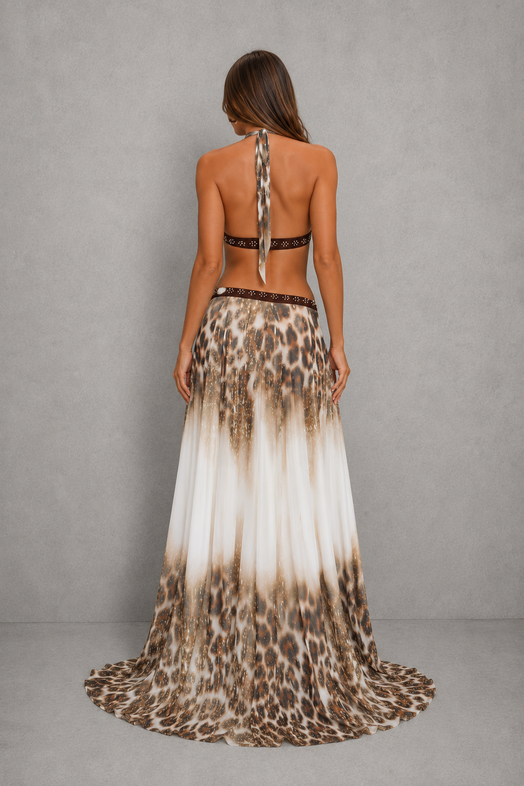 A woman shown from the back wearing a sleeveless, open-back maxi dress with a leopard print pattern that fades into a white gradient at the hem, set against a neutral gray studio background.