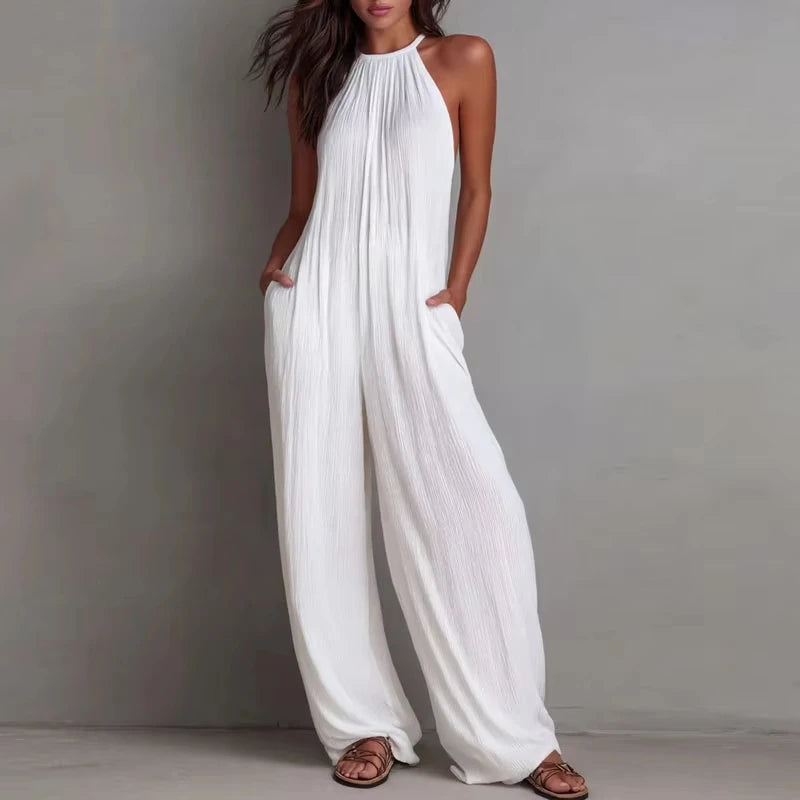 Woman wearing a white halter neck jumpsuit against a gray background