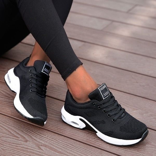 Black athletic shoes with white soles worn on a wooden floor