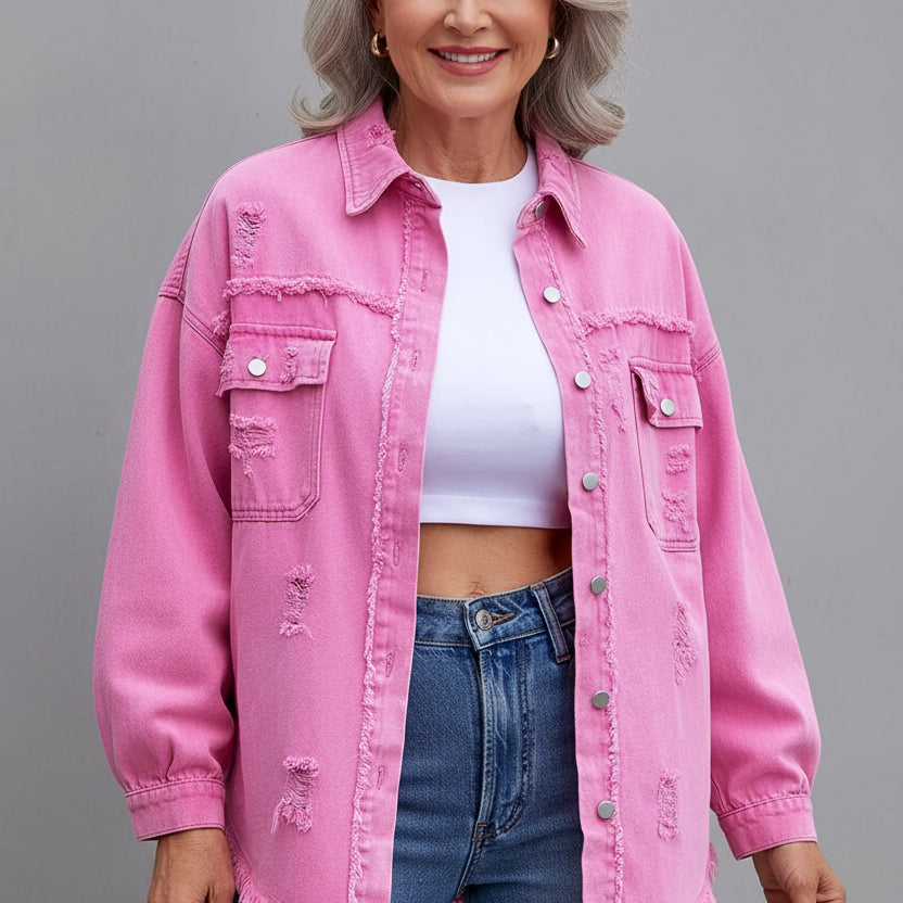 Person wearing a pink distressed denim jacket over a white top and blue jeans on a gray background