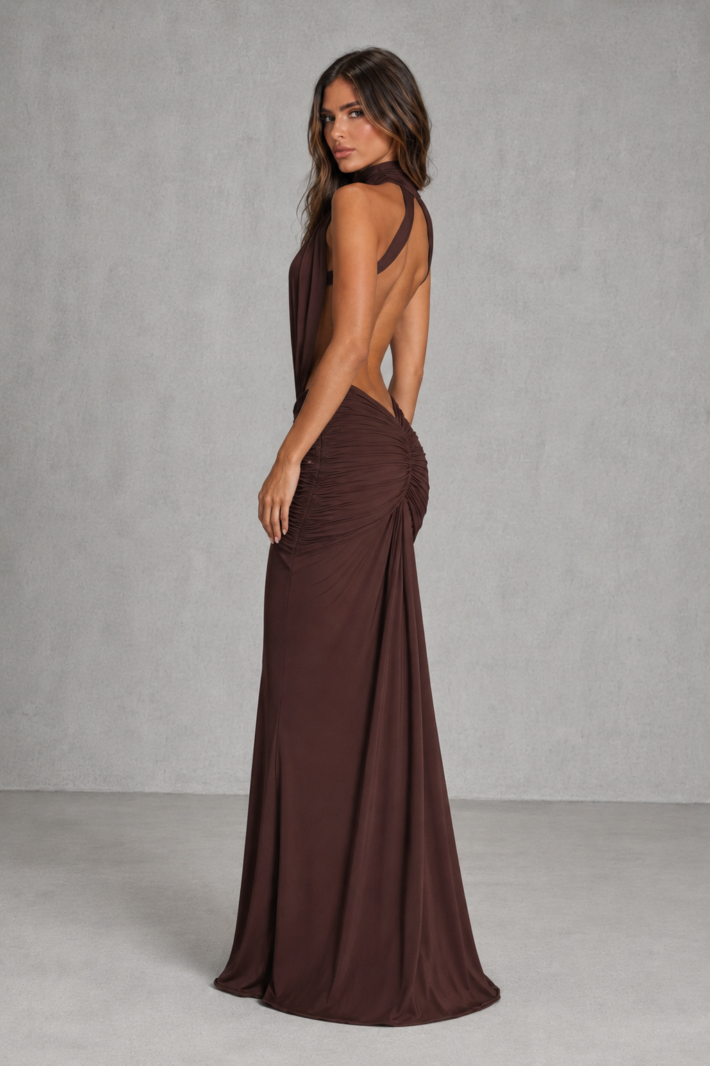 Woman wearing a brown evening gown with a backless design against a gray background