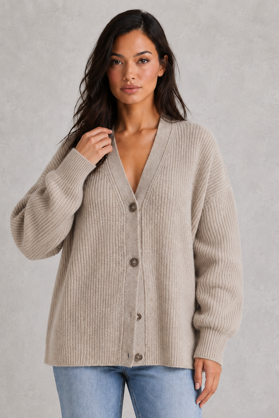 Woman wearing a beige cardigan over a deep neckline top with light blue jeans on a gray background