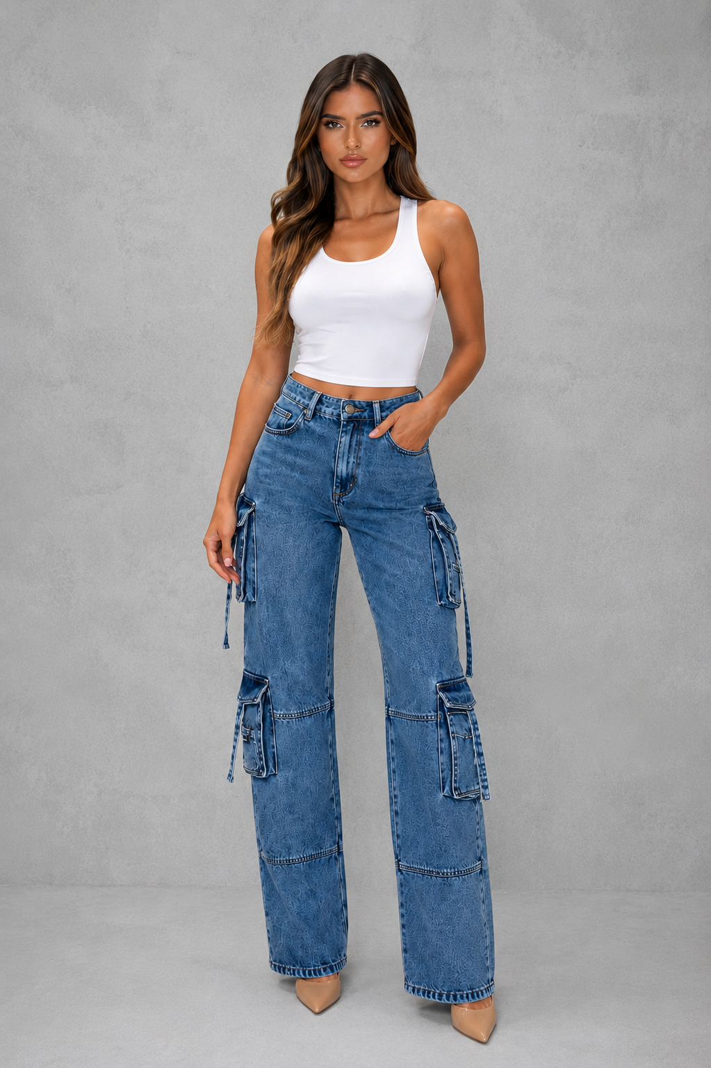 Woman wearing blue cargo jeans and a white tank top on a gray background