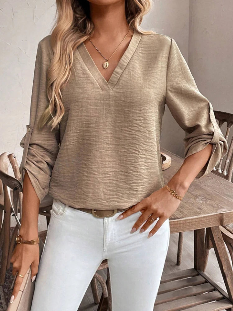 Woman wearing a beige long-sleeve top and white pants in a casual setting.
