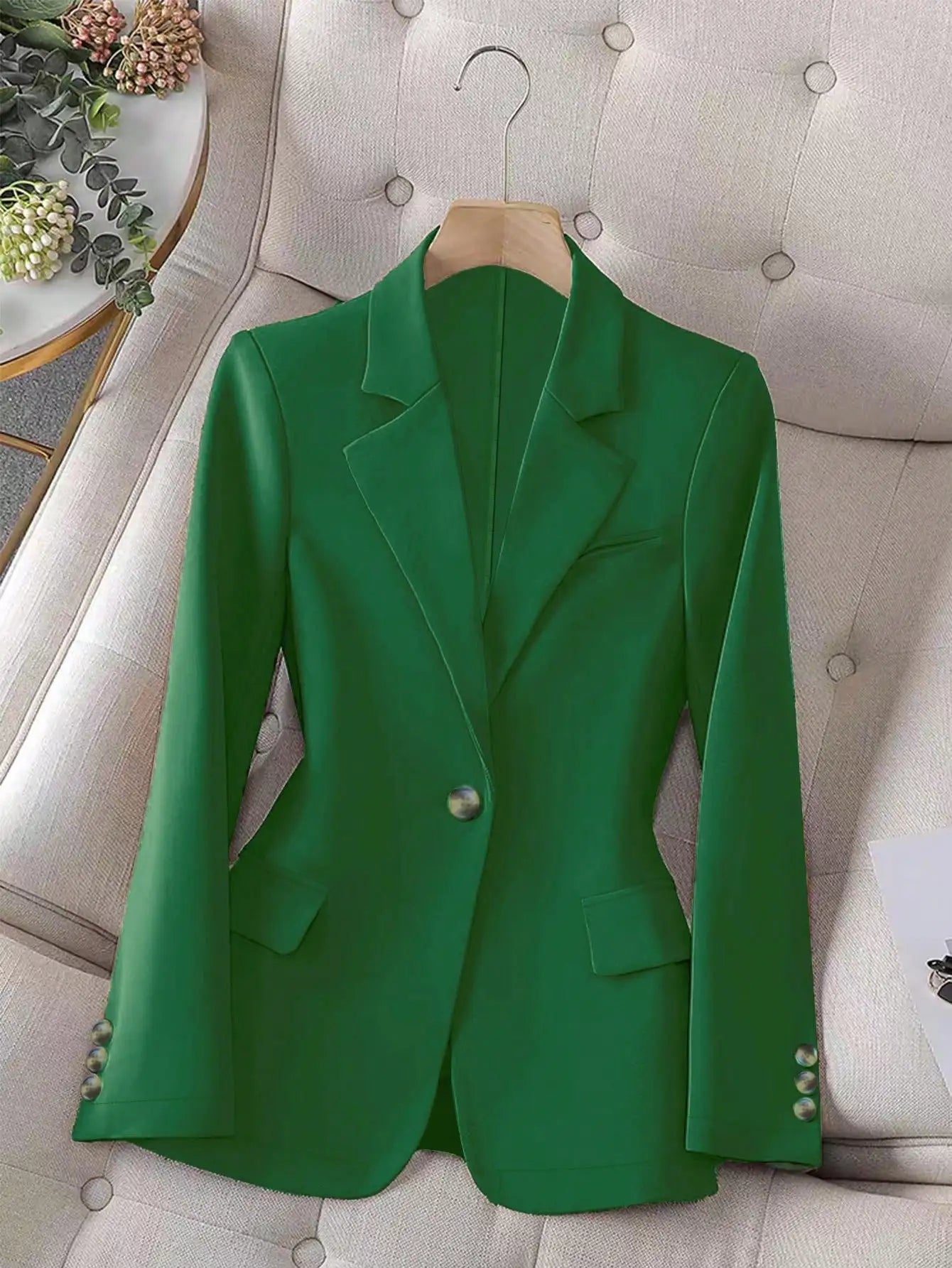 Green blazer on a hanger against a neutral background
