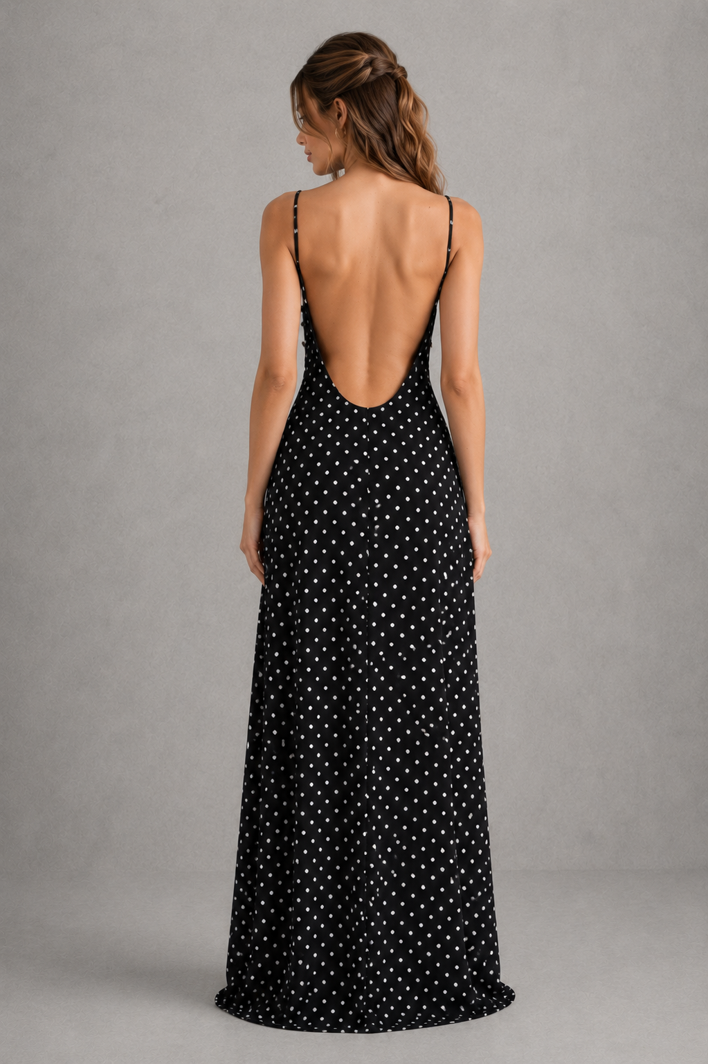 Woman wearing a black polka dot dress with an open back against a gray background