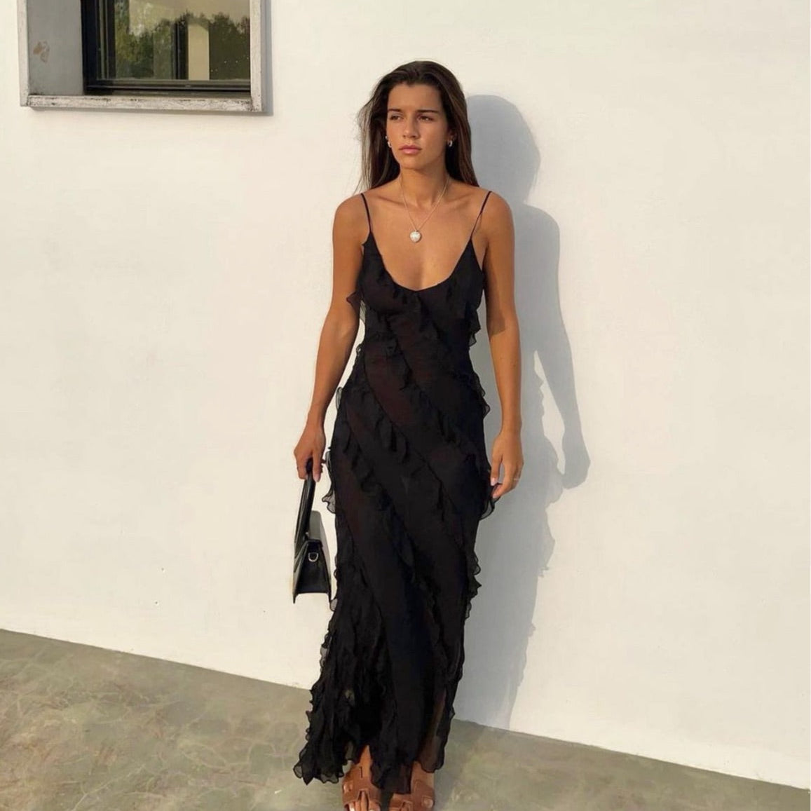 Woman wearing a black ruffled dress against a white wall.