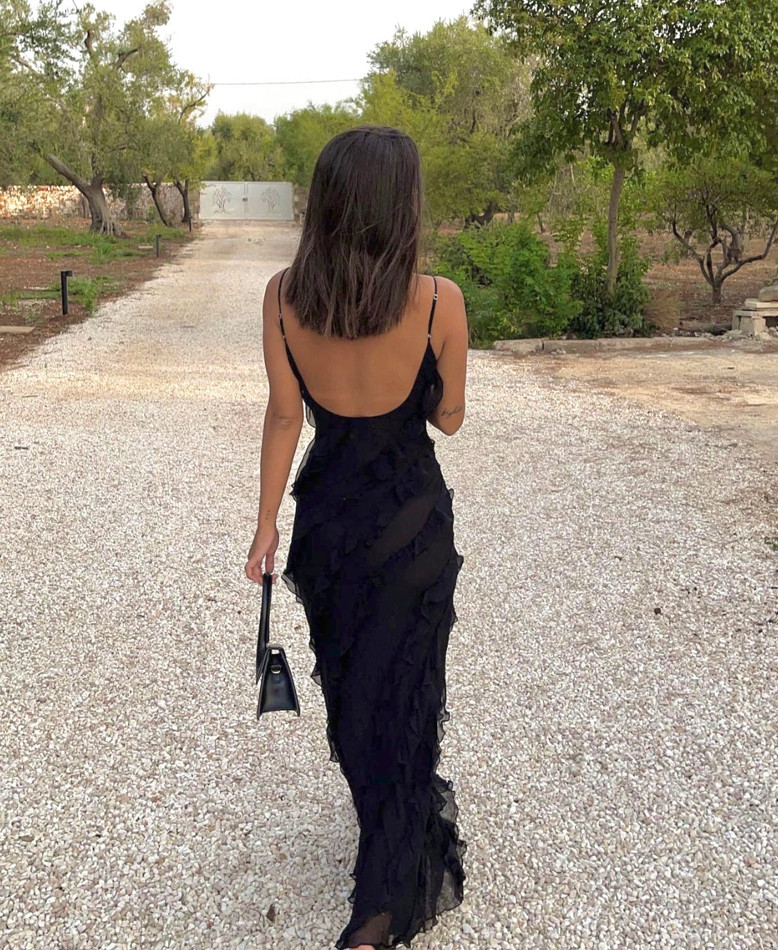 Woman in a black dress walking on a gravel path with trees in the background
