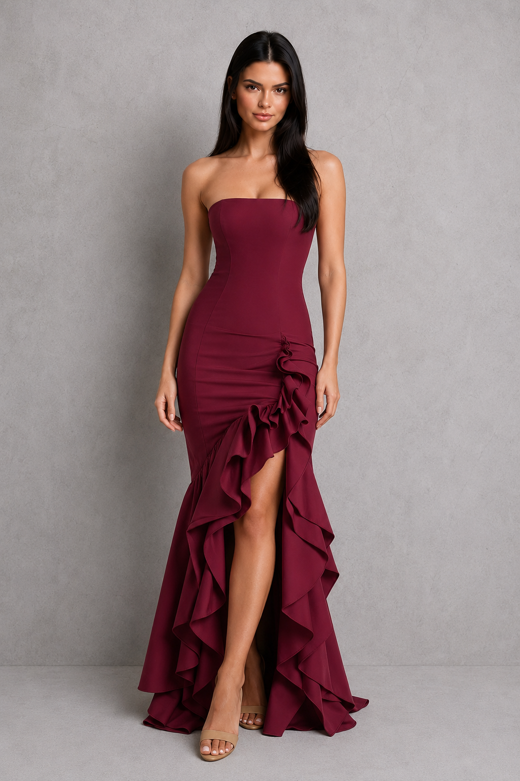Woman wearing a burgundy strapless gown with ruffle details against a gray background