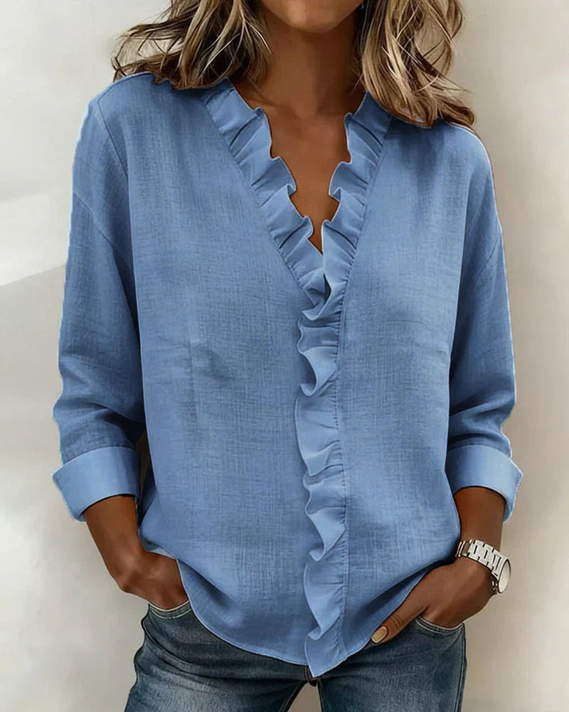 Woman wearing a blue blouse with ruffled details on a plain background