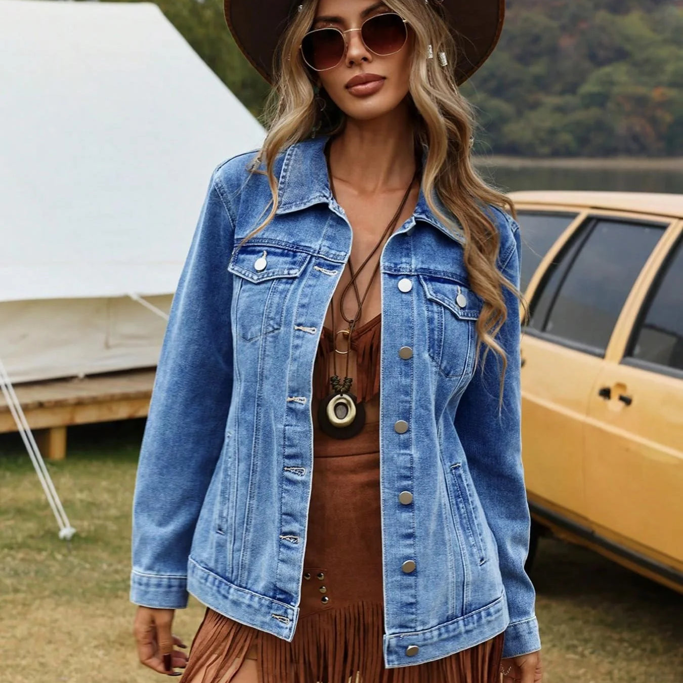 Woman wearing a denim jacket and brown hat outdoors with a tent and vehicle in the background