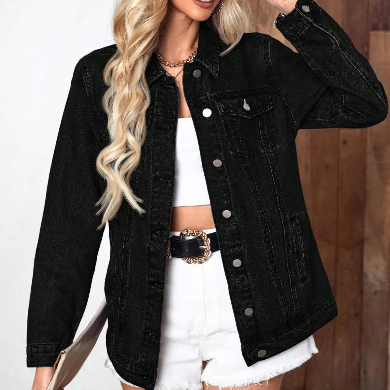 Woman wearing a black denim jacket over a white outfit, holding sunglasses.