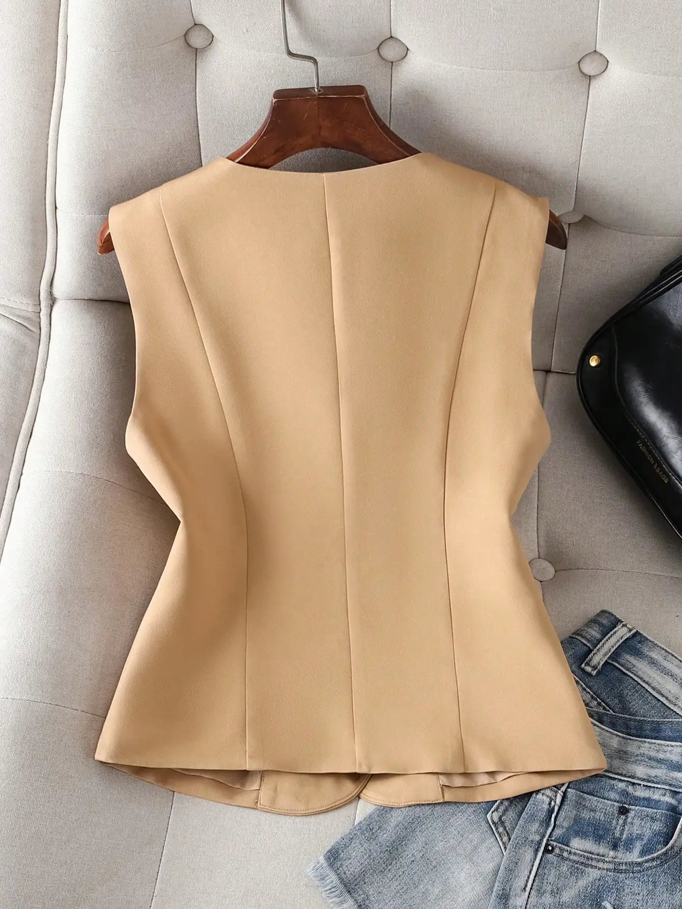 Beige sleeveless top on a hanger with jeans and a black bag in the background.