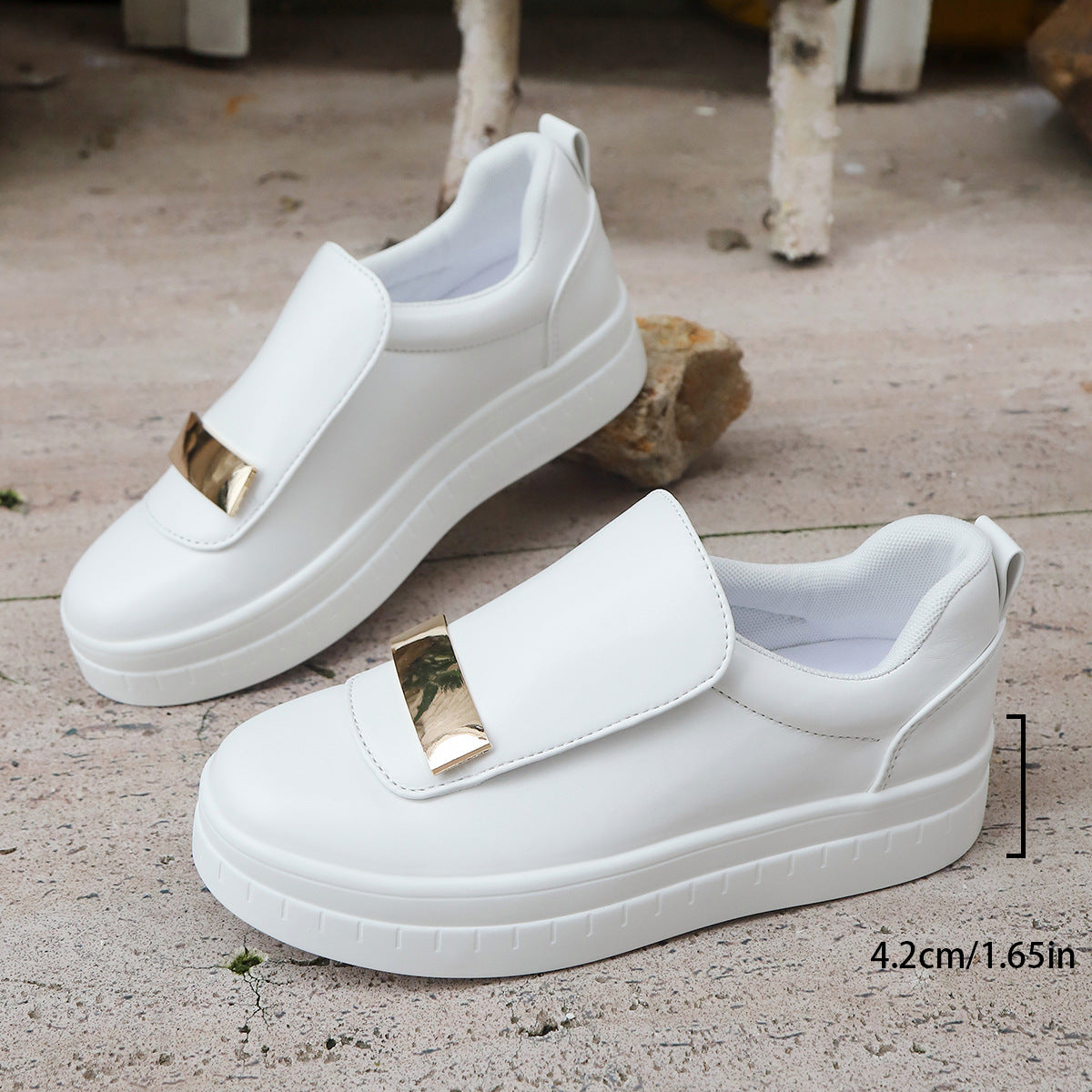 White slip-on shoes with gold accents on a concrete surface.