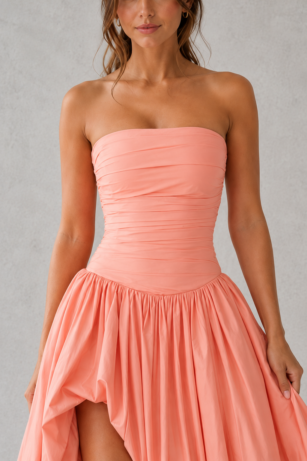 Woman wearing a strapless coral dress against a gray background