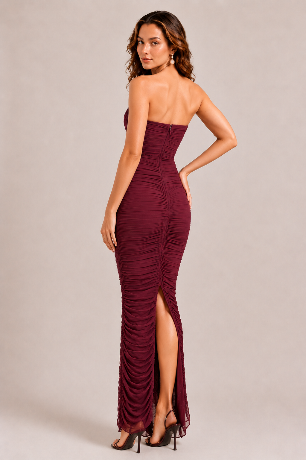 Woman wearing a burgundy strapless gown with a slit on a beige background