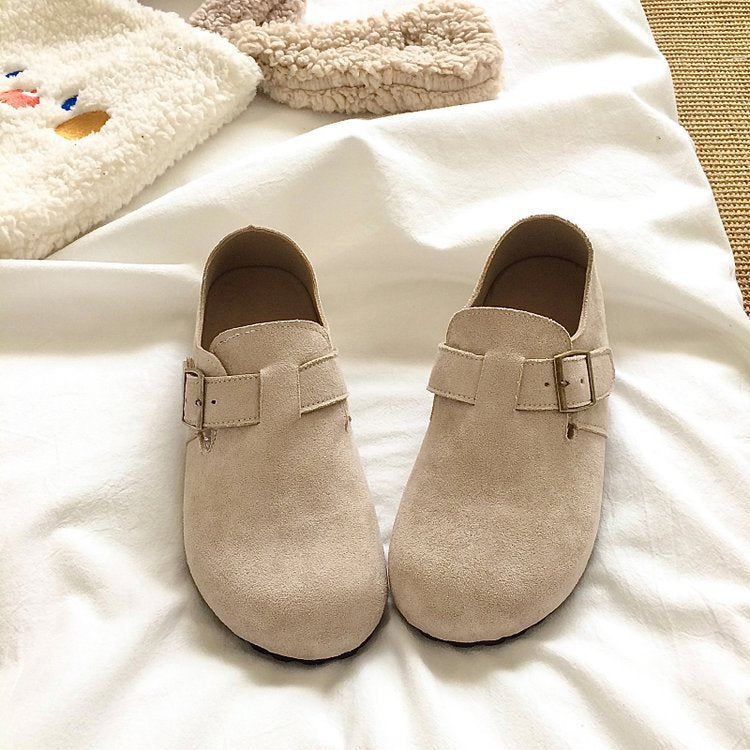 Pair of beige clogs with buckles on a white surface
