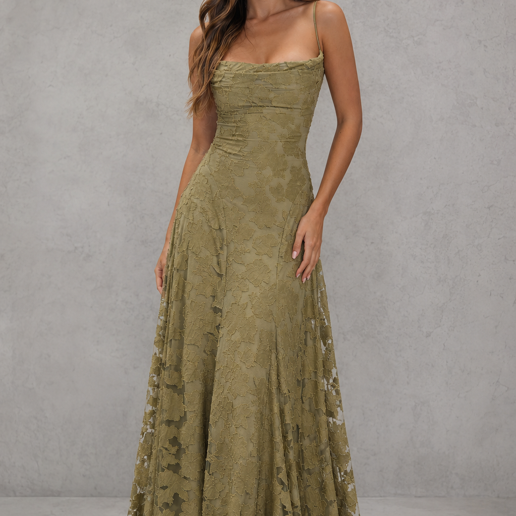 A woman modeling a floor-length olive green strapless gown with a fitted bodice and sheer floral lace side panels, standing against a textured gray studio backdrop.