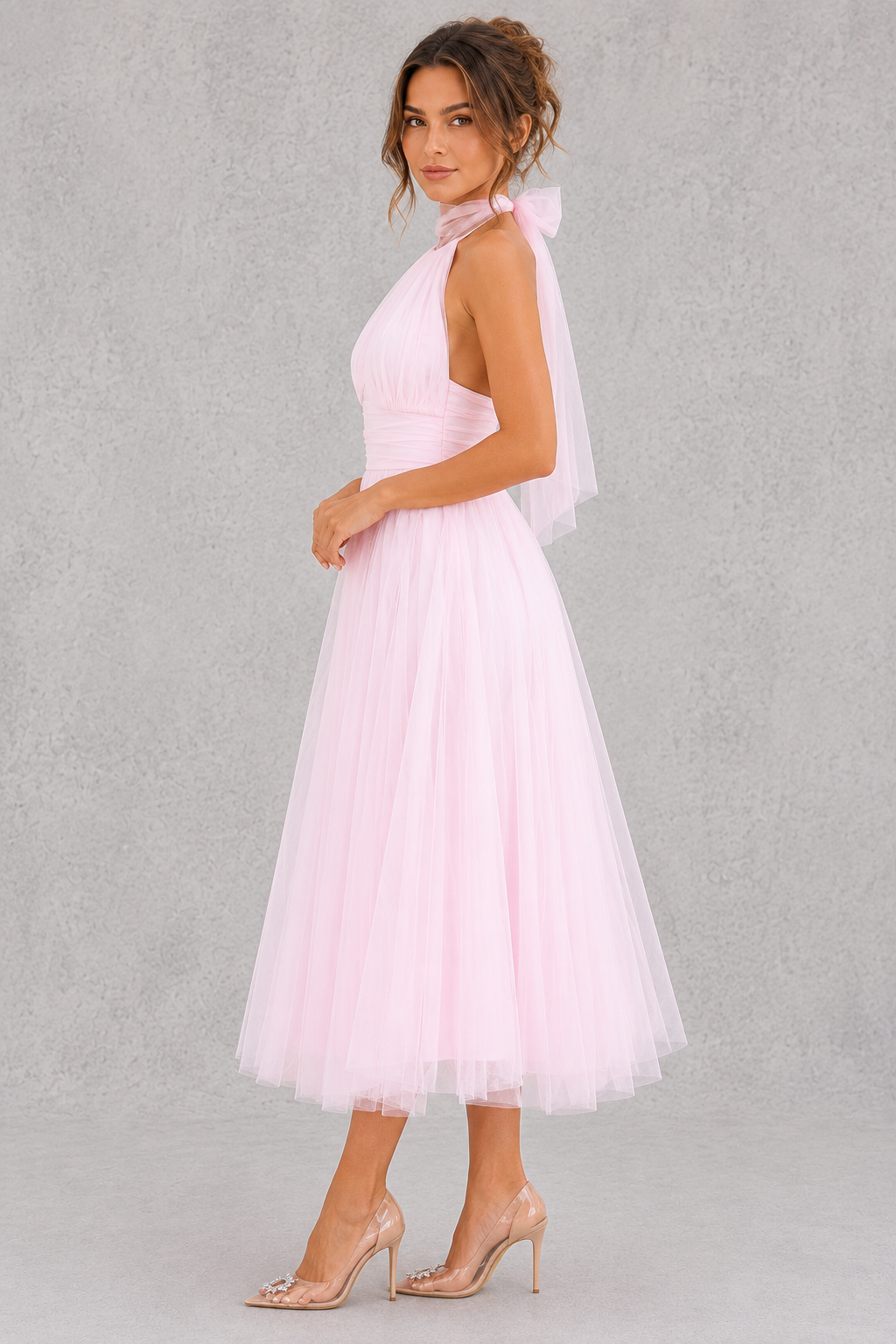 Woman wearing a pink dress with a sheer overlay against a gray background