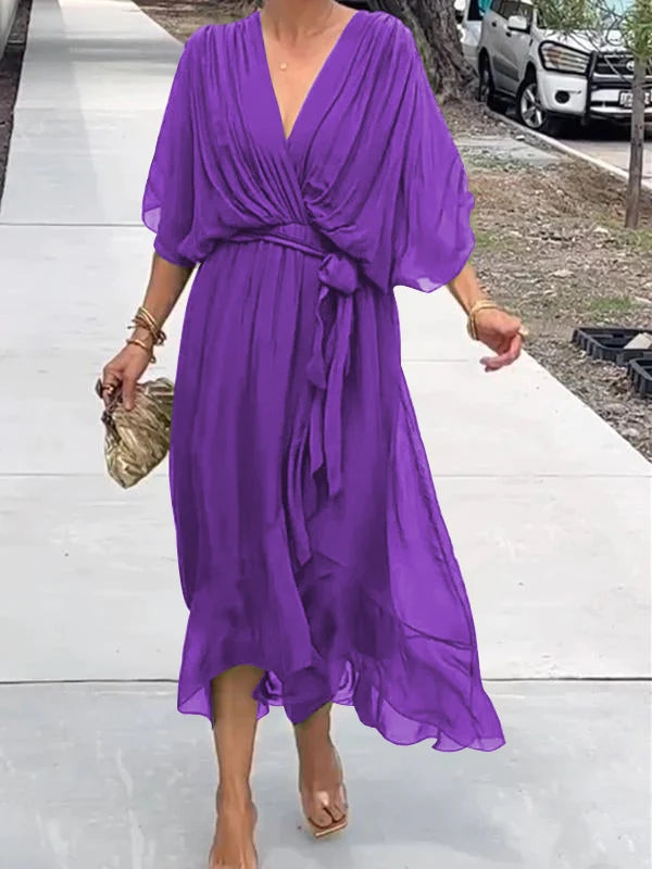 Person wearing a purple dress standing on a sidewalk.