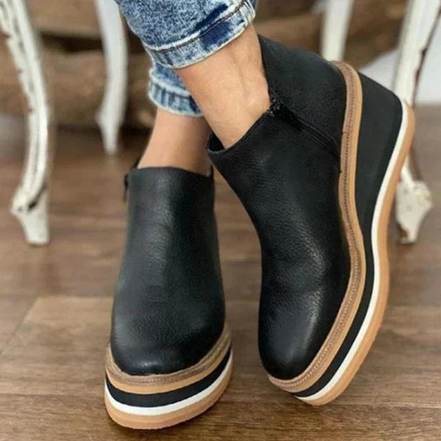 Black platform ankle boots with brown soles worn indoors on a wooden floor.