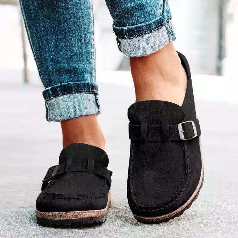 Black loafers with buckles worn with rolled-up jeans on a light background