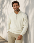 Man wearing a white sweater and beige pants against a light background