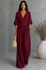 Woman wearing a burgundy dress holding a woven handbag against a gray background
