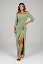 Woman wearing a green off-shoulder dress with a slit on a white background