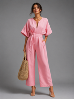Woman wearing a pink jumpsuit holding a woven bag against a gray background