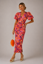 Woman wearing a colorful floral dress with puff sleeves against a plain background