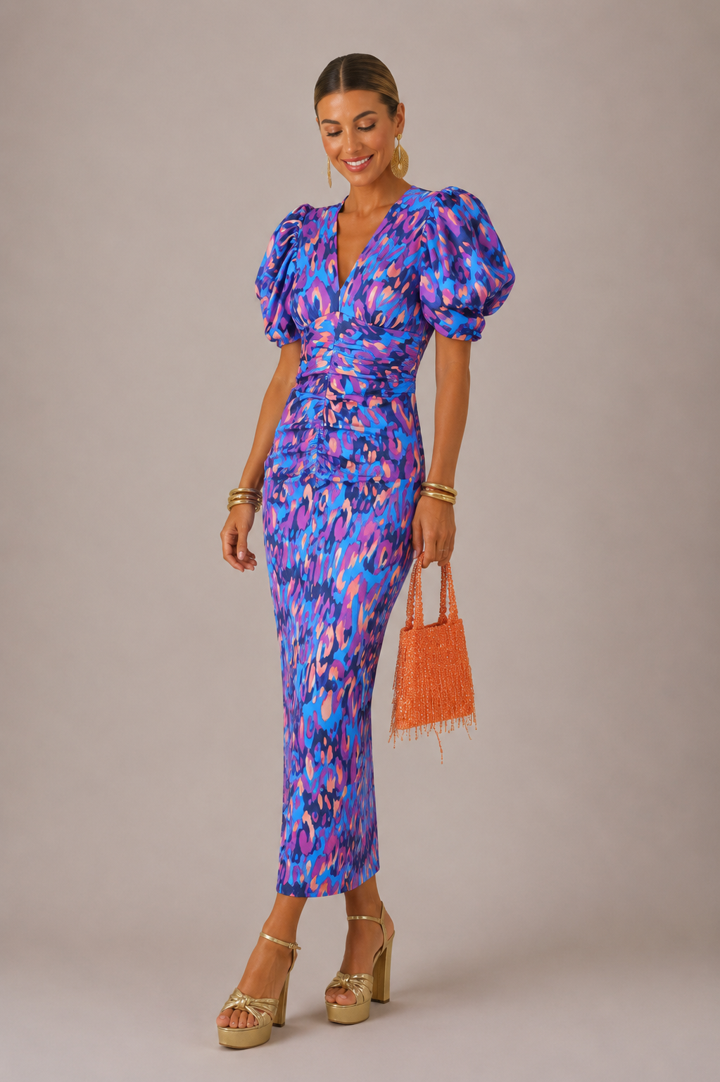 Woman wearing a blue and pink patterned dress with puff sleeves, holding an orange handbag on a beige background.
