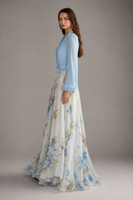 Woman wearing a light blue top and floral skirt against a neutral background