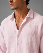 Close-up of a man wearing a light pink textured shirt against a gray background