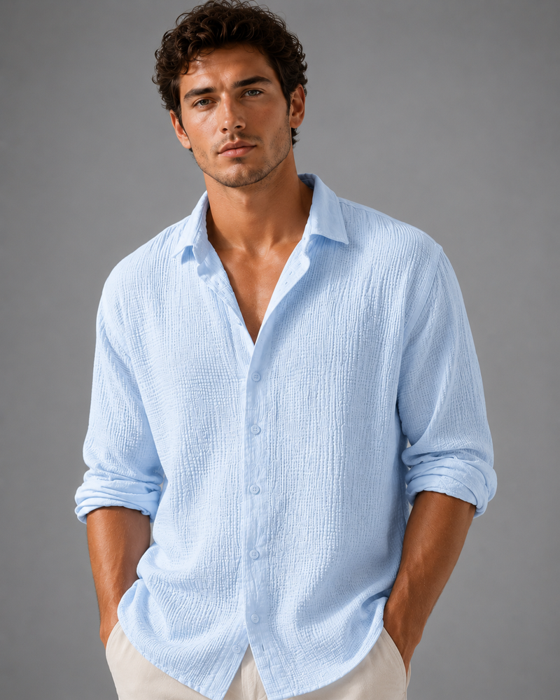 Man wearing a light blue shirt with rolled-up sleeves against a gray background