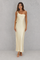 Woman wearing a beige one-shoulder dress against a gray background