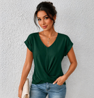 Woman wearing a green top and blue jeans against a white wall