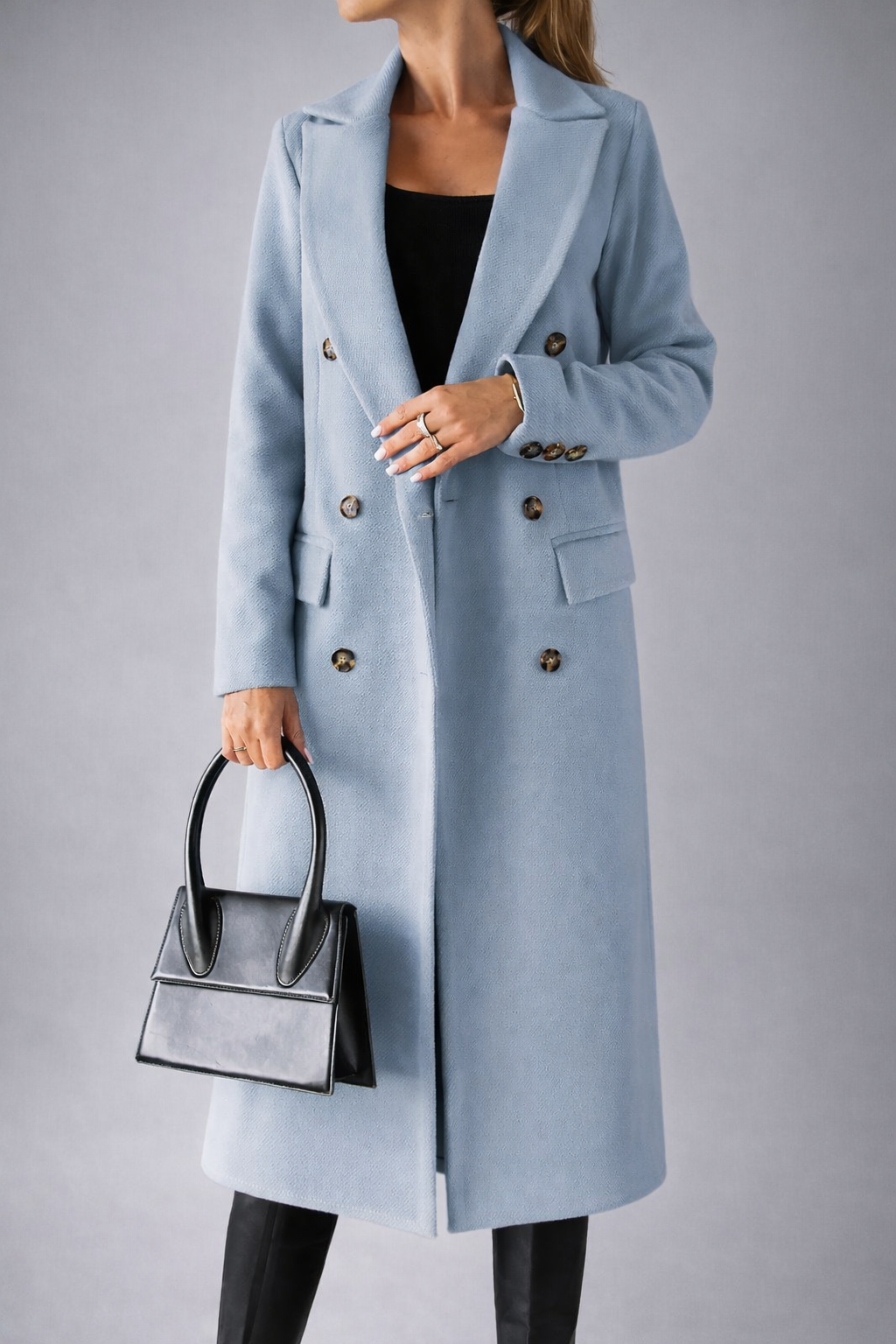 Person wearing a light blue coat with a black handbag on a gray background
