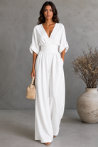 Woman wearing a white dress holding a woven bag against a gray background