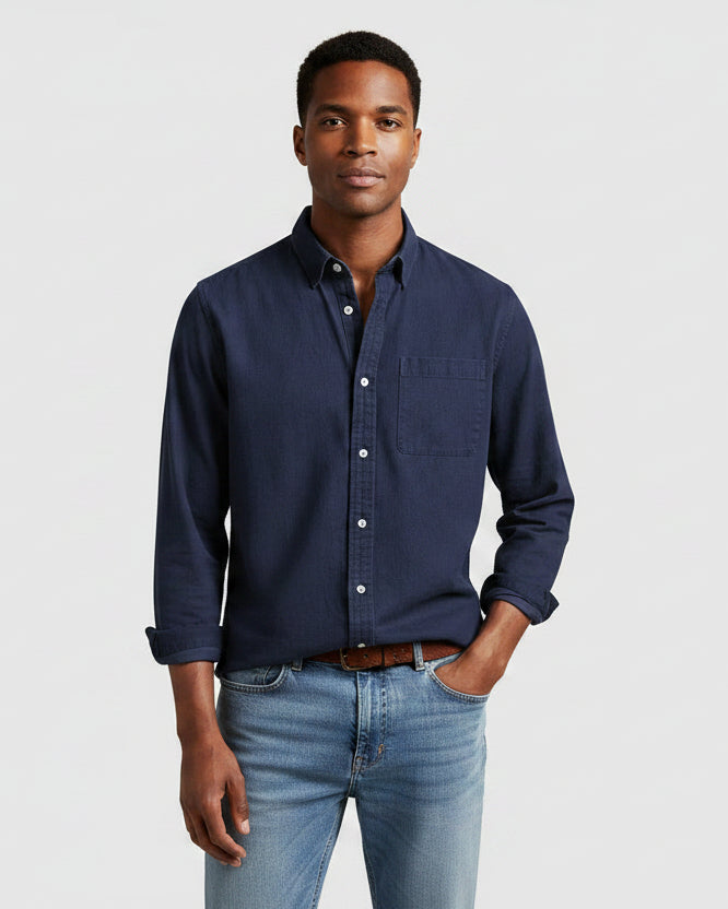 Man wearing a navy button-up shirt and light blue jeans on a white background