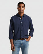 Man wearing a navy button-up shirt and light blue jeans on a white background