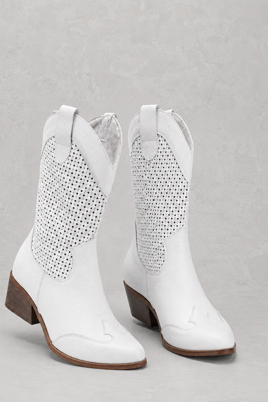 White cowboy boots with perforated design on a gray background