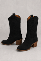 Black cowboy boots with brown soles on a light gray background