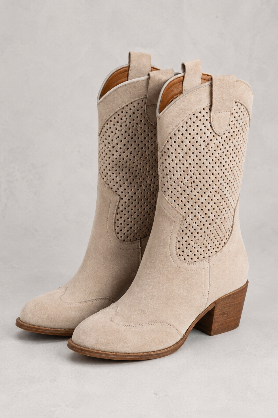 Beige cowboy boots with perforated design on a light gray background