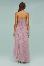 Woman wearing a pink strapless gown with ruffled details on a light gray background