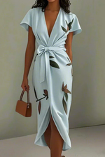 Woman wearing a light blue dress with floral patterns and holding a brown handbag against a plain background