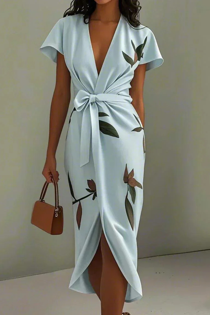 Woman wearing a light blue dress with floral patterns and holding a brown handbag against a plain background